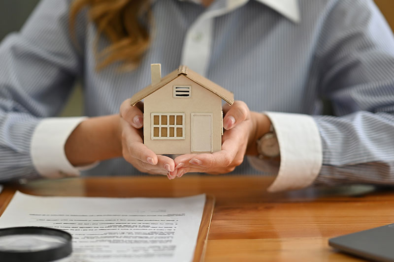 Immobilienmaklerin haelt ein kleines Haus in den Händen